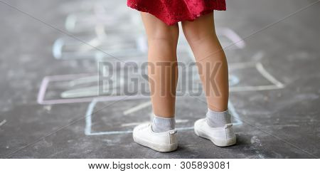 Closeup Of Little Girl's Legs And Hopscotch Drawn On Asphalt. Child Playing Hopscotch Game On Playgr