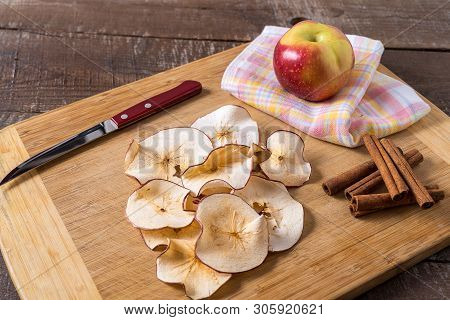 Front View Dried Apple Chips , Raw Apple , Cinnamon Sticks On Cooking Board Over Wood Background.