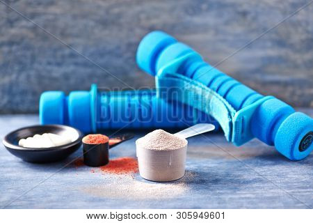 Creatine Powder, Scoop Of Whey Protein, Taurine Capsules And Blue Dumbbells In Background. Sport Nut