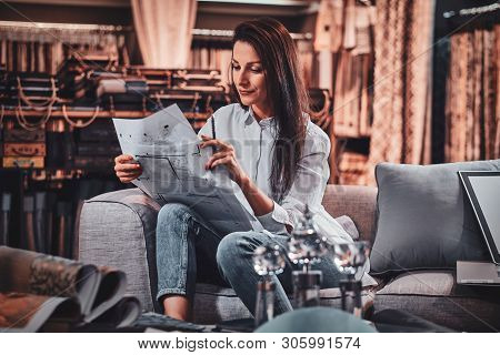 Attractive Pensive Woman Is Sitting On The Sofa At Her Curtians Atelier While Handing Drawings About