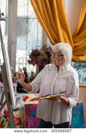 Blonde-haired Retired Artist Standing Near Window And Painting