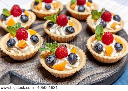 Fruit And Berry Tartlets Dessert Assorted On Wooden Tray. Closeup Of Delicious Pastry Sweets Pies Co