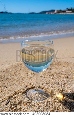 Glass Of Local Dry White Wine On White Sandy Beach And Blue Mediterranean Sea On Background, Near Le