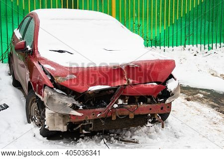 Rred Passenger Car With A Broken Front Part In A Parking Lot Covered With Snow