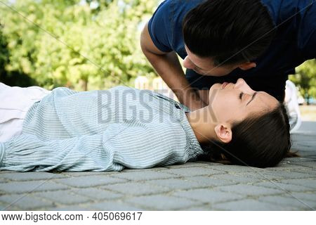 Man Checking For Breathing Of Unconscious Young Woman Outdoors