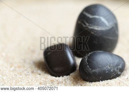 Three black stones in the sand.