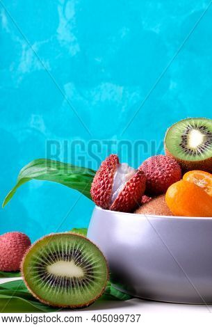 Lychee, Kiwi And Kumquat In A Gray Ceramic Bowl Against The Turquoise Background. Assorted Tropical 