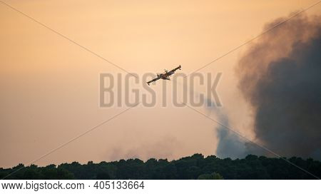 Amphibious water bomber dropping water on fire, smoke from the forest fire, in France.