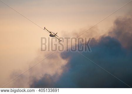 Amphibious water bomber airplane in flight at sunset, smoke from a forest fire, in France.