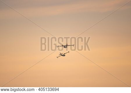 Two amphibious water bomber airplanes in flight at sunset, in France.