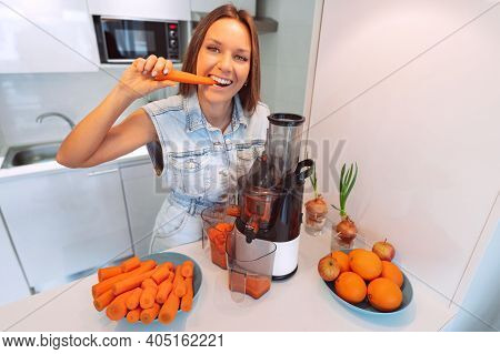 Happy Healthy Woman Making Fresh Carrot Juice In A Juicer In The Kitchen At Home. Juicer And Homemad