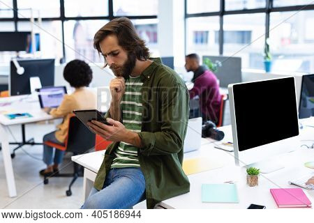 Caucasian businessman leaning on desk using tablet computer in creative office. business people and work colleagues at a busy creative office.