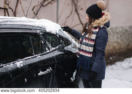 A Woman Is Cleaning Snowy Window On A Car With Snow Scraper. Pretty Woman Warmy Dressed Clean Her Ca