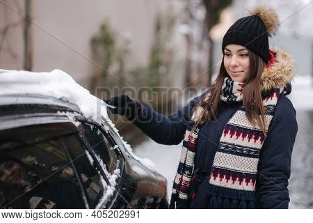 A Woman Is Cleaning Snowy Window On A Car With Snow Scraper. Pretty Woman Warmy Dressed Clean Her Ca