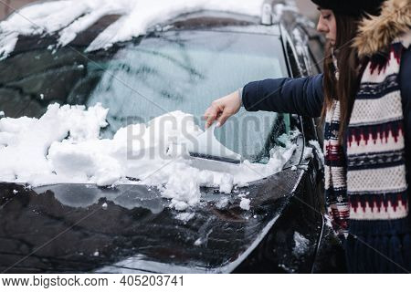 A Woman Is Cleaning Snowy Window On A Car With Snow Scraper. Pretty Woman Warmy Dressed Clean Her Ca