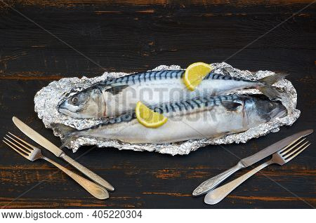 Two Mackerel Fishes Ready For Cooking Decorated With Lemon Slices On The Black Wooden Table. Top Vie