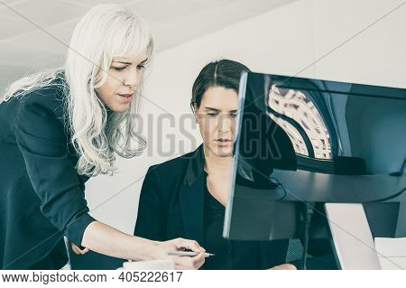 Female Boss Affixing Signature On Managers Report. Businesswomen Sitting And Standing At Workplace W