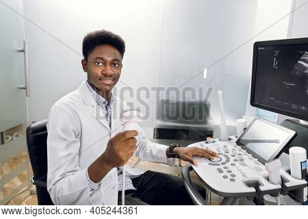 Smiling African Man Doctor With Ultrasound Transducer In Hand, Working On Modern Ultrasound Scanning
