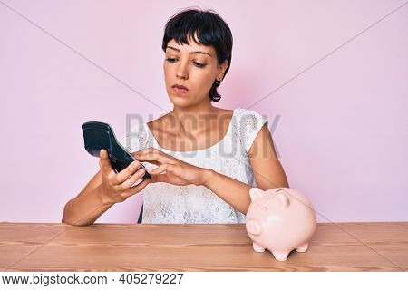 Beautiful brunettte woman caculating money savings relaxed with serious expression on face. simple and natural looking at the camera. 