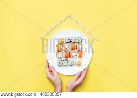 Female Hands Hold A White Plate With Rolls And Sushi On A Disposable Background. Home Delivery Conce