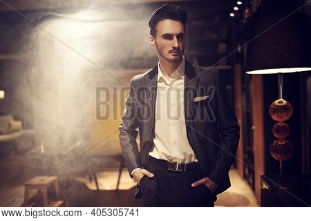 Handsome brunet man in an elegant suit stands in a luxury apartment. Mafia. Male beauty, fashion.