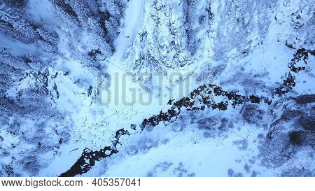 A Majestic Snowy Gorge With Fir Trees In Mountains. Tall Trees Brush Against White Clouds. Steep Cli
