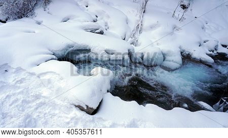 A Clear Mountain River Runs Through A Snowy Gorge. There Is A Metal Bridge Covered With Snow. Tall S