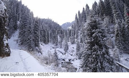 A Clear Mountain River Runs Through A Snowy Gorge. There Is A Metal Bridge Covered With Snow. Tall S