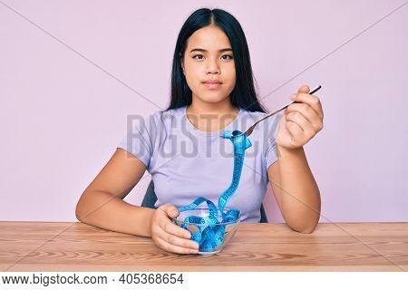 Young asian girl eating measure meter doing diet for weight loss relaxed with serious expression on face. simple and natural looking at the camera. 