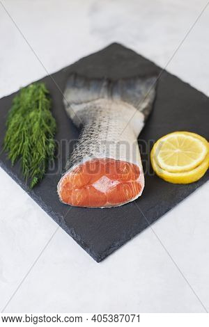 Fresh Raw Salmon Tail Fillet Part With Lemon And Dill Served On A Black Stone Board On Light Backgro