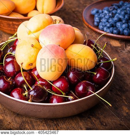 Bowl With Berries Cherries And Apricots On An Old Wooden Rustic Table Close-up Against A Background 