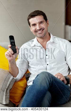 Front Portrait Of A Handsome Smiling Man Looking At Cameraa Holding In Hands A Stationary Phone Sitt