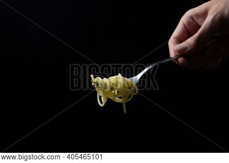 Spaghetti On A Black Background. Boiled Spaghetti On A Fork. Isolated Spaghetti. Male Hand Holding A