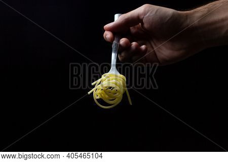 Spaghetti On A Black Background. Boiled Spaghetti On A Fork. Isolated Spaghetti. Male Hand Holding A