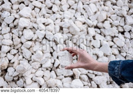 Hand Holds A White Chalkstone With A Lot Of Stones On The Background