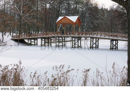Scenic Winter Landscape View Of Old Wooden Bridge Over The Frozen Lake In The Village Of Pushcha-vod