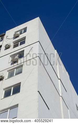 A Fragment Of A Tall Residential Building Against A Clear Blue Sky. A White Apartment Building. View