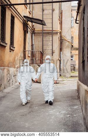 Doctors In Protective Suits And Protective Masks Stand On The Street With Serious Faces. Walking Alo