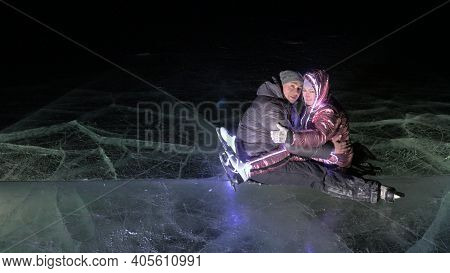 Young Loving Couple Skating At Ice Rink At Night. Man And Woman Kiss Hug Have Fun Learn To Skate. Ma