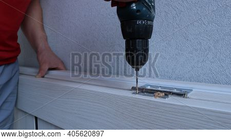 Fixing The Metal Fastening On The Door Leaf By A Carpenter Using A Screwdriver, A Man Twists A Self-