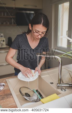 Young Woman Standing By The Kitchen Sink, Washing The Dishes After Lunch; Woman Doing The Washing Up