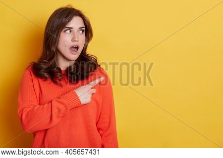 Portrait Of Shocked Caucasian Female With Pleasant Appearance Indicates Aside At Blank Yellow Wall, 