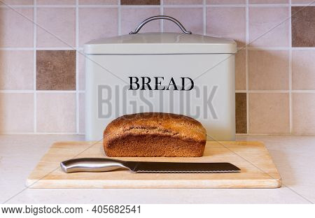 A Loaf Of Freshly Baked Wholemeal Bread Sits On A Bread Board In Front Of A Storage Tin With Knife R