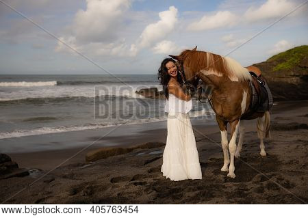 Happy Smiling Woman Leading Horse By Its Reins. Horse Riding On The Beach. Human And Animals Relatio