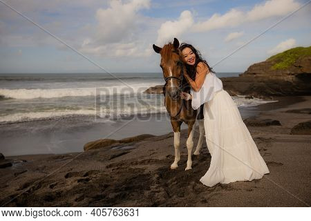 Beautiful Smiling Woman Leading Horse By Its Reins. Cuddling Horse. Love To Animals. Asian Woman Wea
