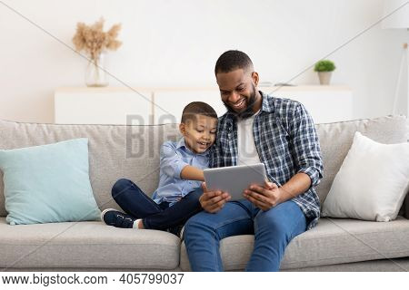 Young Black Father And Little Son Using Tablet Browsing Internet Together And Watching Movie Online 