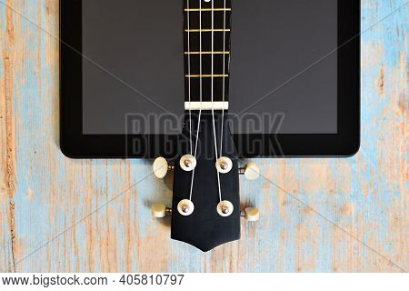 Tablet And Ukulele On Wooden Table With Space For Text. Online Learning To Play Hawaiian Guitar. Uku