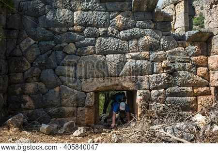 Hiking Lycian way. Man is trekking through low doorway of Pydnai Ruins, well-preserved polygonal masonry Pydnai was small naval and military base fortress, Outdoor activity in Turkey