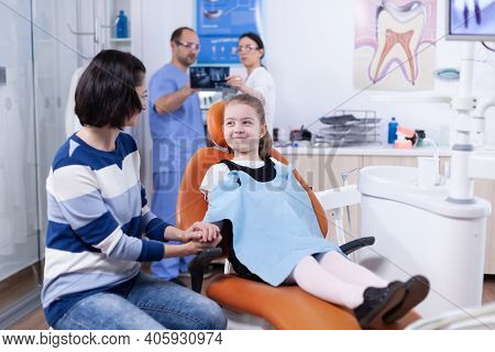 Happy Little Girl Wearing Dental Bib In Dentist Office Holding Parent Hand Waiting Tooth Examination