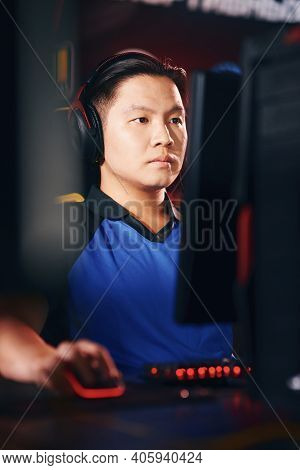 Vertical Shot Of Concentrated Asian Guy, Male Cyber Sport Gamer Wearing Headphones Looking At Pc Scr